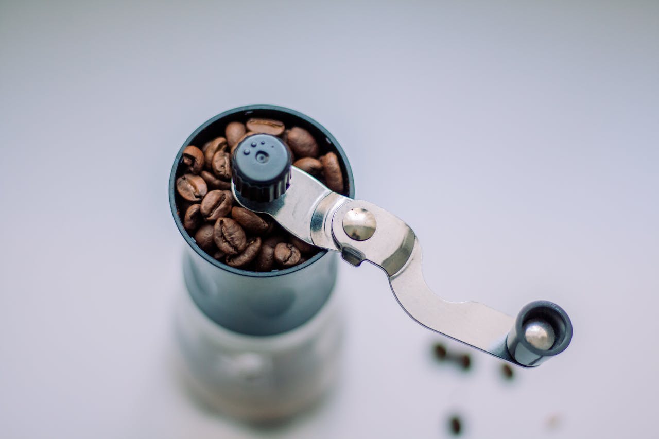 Overhead shot of a manual coffee grinder filled with whole coffee beans.